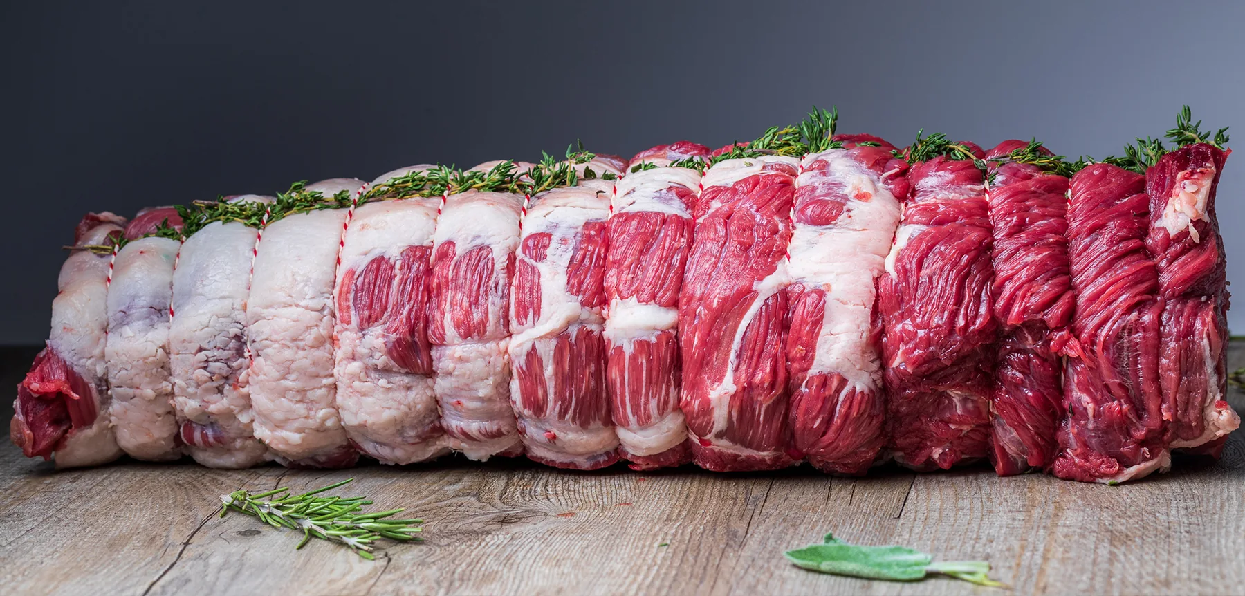 Brisket de vită lung, legat cu sfoară și presărat cu cimbru, pe o masă de lemn