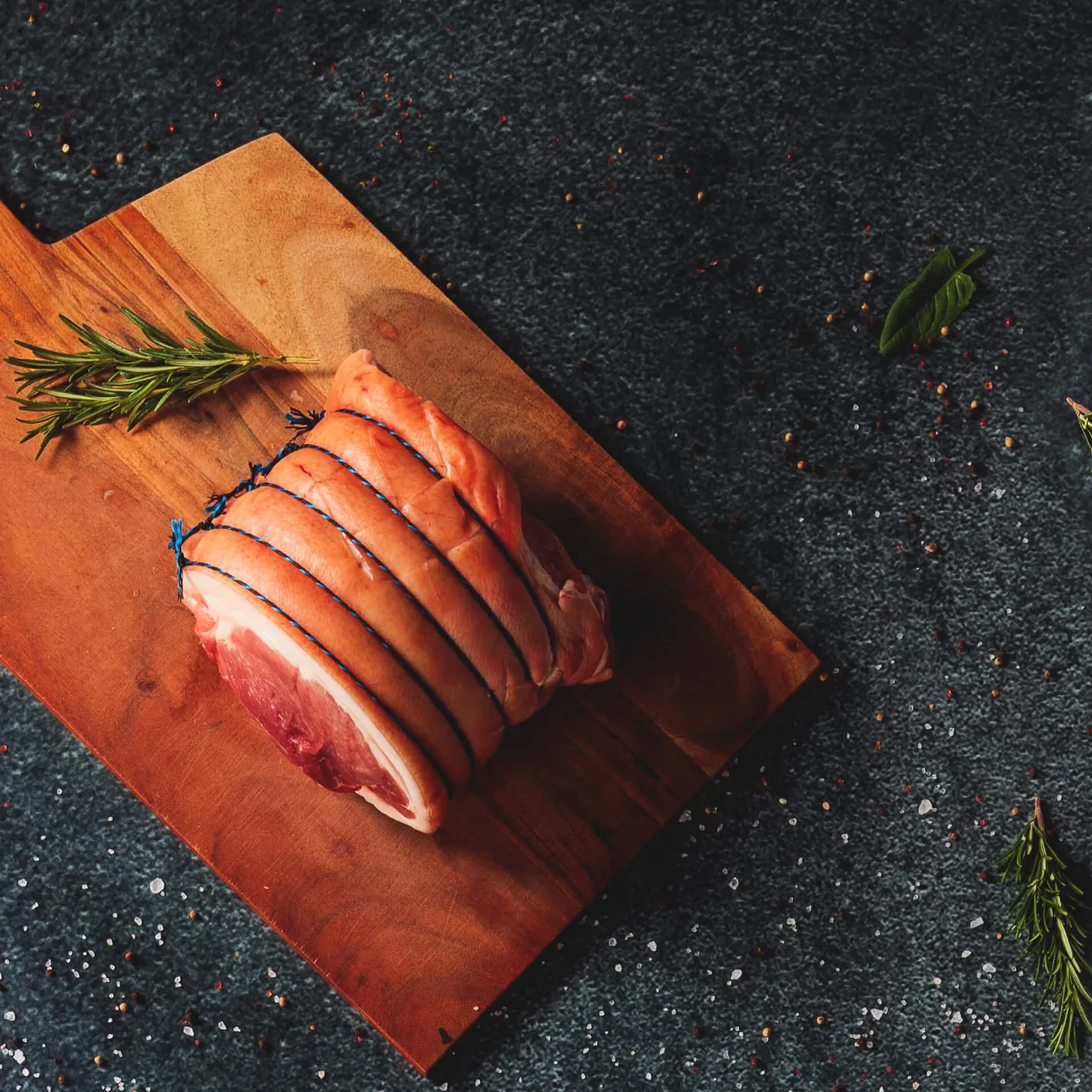 Rulou de pulpă de porc legat cu sfoară, pe un tocător de lemn, cu rozmarin alături